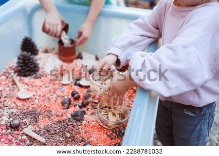 Children playing at a sensory bin with coloured grains, pretending to cook