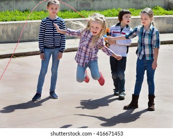 Children playing skipping rope jumping game and laughing outdoors