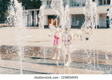 Children Playing With Small Fountains On The Urban Plaza. Blurred Background