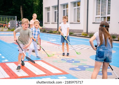 Children Playing Street Hockey On A City Holiday On The Playground. Happy Kids Group Have Fun. Summer Activites For Children Concept.