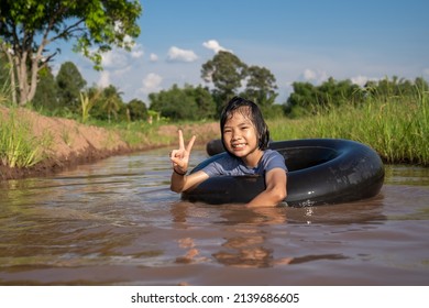 Children Playing And Swimming In Canal Of Organic Farm Agriculture In Rural, Happy Kids Floating And Funny In Water By Ring Rubber Tire In Countryside, Sustainable People Lifestyle In Rural