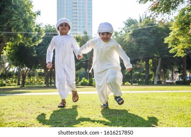 Children playing together in Dubai in the park. Group of kids wearing traditional kandura white dress from arab emirates