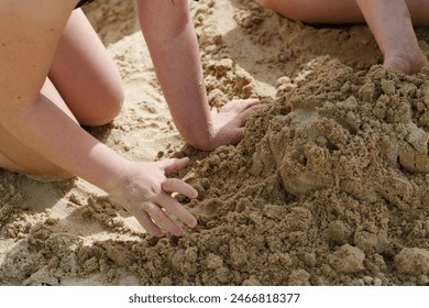 Children playing in wet sand on a sunny beach. Two children are engaged in building a sandcastle on a sunny beach afternoon. They use their hands to mold the sand and create shapes. Summer background - Powered by Shutterstock