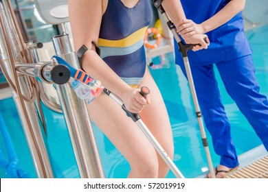 Children Pool Rehabilitation. Practitioner Physician Helping Disabled Girl To Reach The Swimming Pool By Special Chair Lift. Caucasian Disabled Girl. Physical Therapy Concept Photo.