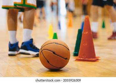 Children Practicing Basketball on School Court. Basketball Training Game Background. Basketball and Training Cones on Wooden Floor Close Up with Blurred Players Playing Basketball Game in Background