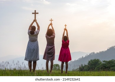 Children praying to the GOD while holding a crucifix symbol with bright sunbeam on the mountain