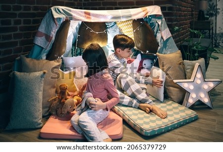Children preparing tent with chairs and bed sheets for pajama party