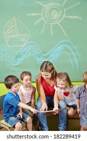 Children In Preschool Reading Book Together With A Nursery Teacher