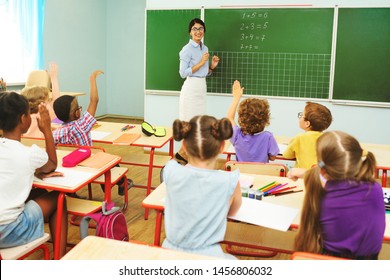 children preschoolers pull up their hands to answer the teacher's question on the background of the blackboard and the classroom in primary school. Back to school, education - Powered by Shutterstock