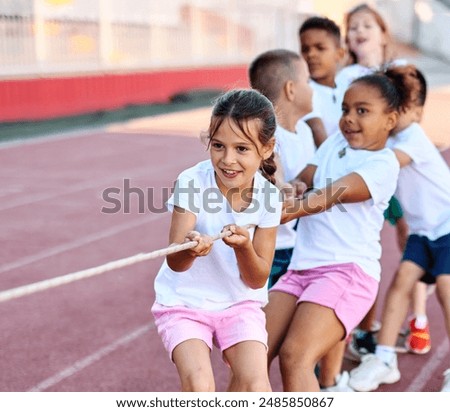 Children pulling a rope at the stadium, practice during sports class in school training, little fit boys and girls in sportswear training as athletes outdoor. Concept of sport, fitness and achievement