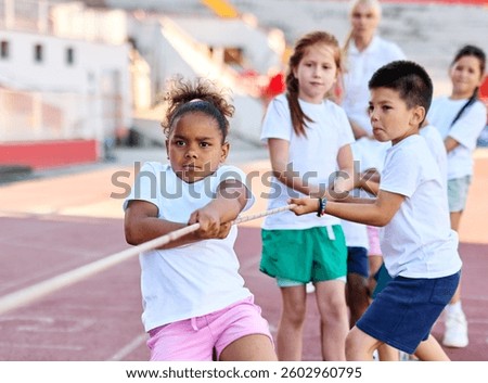Children pulling a rope at the stadium, practice during sports class in school training, little fit boys and girls in sportswear training as athletes outdoor. Concept of sport, fitness  teamwork