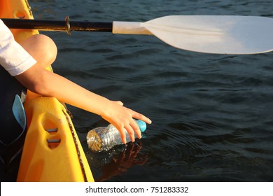 Children are reaching for a bottle of plastic waste in the ocean while paddling a kayaking
