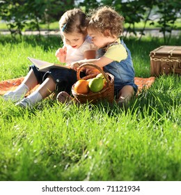 Children Reading The Book On Picnic In Summer Park