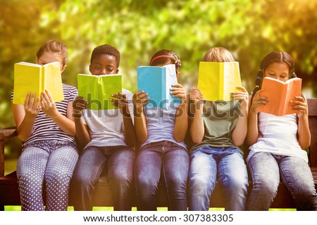 Children reading books at park against trees and meadow in the park