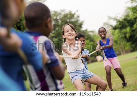 Children and recreation, group of happy multiethnic school kids playing tug-of-war with rope in city park. Summer camp fun