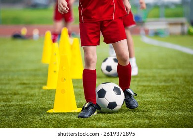 Children in red soccer uniforms practicing dribbling skills around yellow cones on a grassy field during a soccer training session