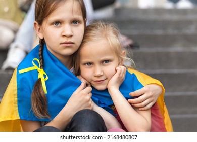 Children Refugee from Ukraine.   Sad Depressed Migrant Children with Ukraine Symbols. Two frightened Girls wrapped in Ukraine Flag. 