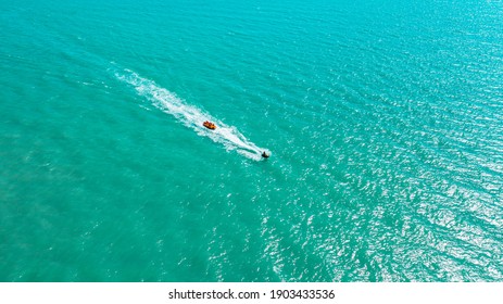 children ride at high speed on the waves in the open sea on an inflatable rubber banana, aerial photography
