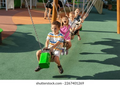 Children ride on a long swing on a modern playground, sit behind each other and laugh - Shutterstock ID 2267401269