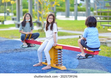 Children Ride On See Saw In Park Playground.Asian Siblings Playing On Healthy Outdoor Recreational Equipment.Childhood And Friendship.Young Girls And Boy Play In School Yard.Climbing.