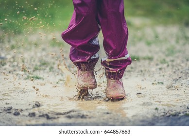 Children in rubber boots and rain clothes jumping in puddle. Water is splashing from girls feet as she is jumping and playing in the rain. Protective rubber pants and jacket for playing in the mud.
