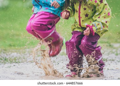 Children in rubber boots and rain clothes jumping in puddle. Water is splashing from girls feet as she is jumping and playing in the rain. Protective rubber pants and jacket for playing in the mud.
