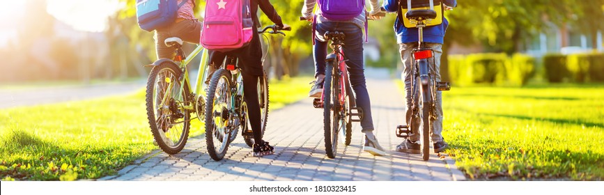 Kinder mit Rucksacksack fahren im Park in der Nähe der Schule. Schüler mit Rucksäcken im Freien