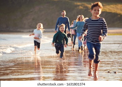 Children Run Ahead As  Multi-Generation Family Walk Along Shore On Winter Beach Vacation