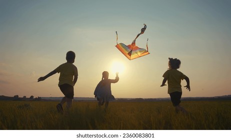 children run with a kite in the park. happy family kid dream concept. a group of children run in the park in nature at sunset playing with kite. kids silhouette play together in park with sun kite