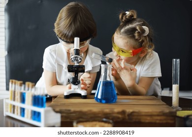 Children scientists. Schoolchildren in laboratory conduct experiments. Boy and girl experiments with a microscope. - Powered by Shutterstock