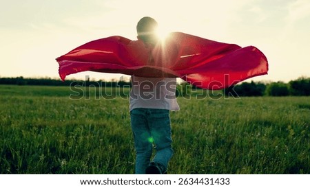 Children self-expression. Superhero boy running on green grass in park. Superhero kid brave boy run in red cape at sunset summer. Boy in superhero costume playing fantasy character flying on meadow