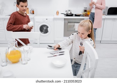 children setting table in kitchen while granny preparing breakfast - Shutterstock ID 2110353023