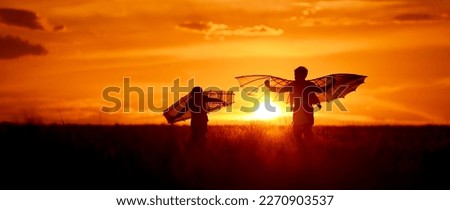 Children silhouettes with wings at sunset. Funny kids run in the meadow on a summer evening. Boys dream of flying and imagine themselves as pilots.