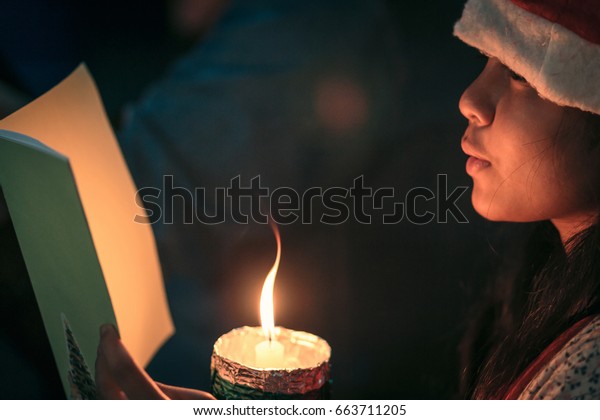A children singer of caroler hands holding\
candle and book with singing carol song on celebration of Christmas\
day background