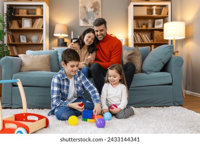 Children sister and brother playing drawing together on floor while young parents relaxing at home on sofa, little boy girl having fun, friendship between siblings, family leisure time in living room - Powered by Shutterstock