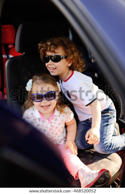 children sit in the car and play. little boy and\
girl in sunglasses laugh in the\
car