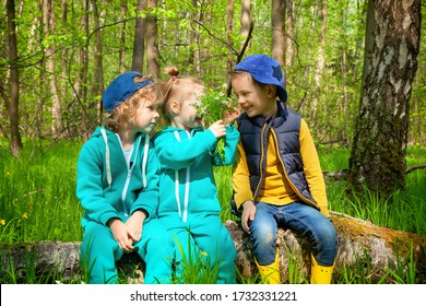 Children Sit On A Log In The Spring Forest. The Girl Gives The Boy A Sniff Of The Bouquet. The First Children's Love. Hiking, Camping, Family Outdoor Activities. Friendship Since Childhood.