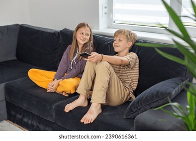 Children sitting on the sofa and watching TV interesting film. Boy holding TV remote. Rest after school. - Powered by Shutterstock