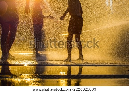  children splashing in the jets of the fountain in the summer heat at sunset
