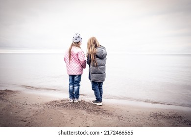 Children stand on the seashore of the lake and look into the distance. Early spring morning cloudy sky. The boy and the girl are dressed in warm clothes. lifestyle. Selective focus
