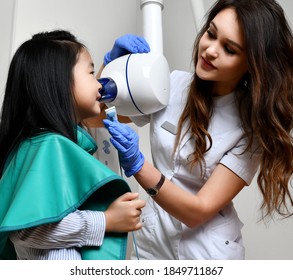 Children Stomatologist Makes Dental Procedure Using  X-ray Machine. Panoramic Radiography For An Asian Child Kid Girl With Special Dentist Equipment In Medical Cabinet