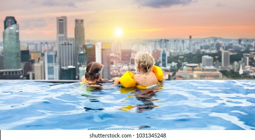Children Swimming In Roof Top Outdoor Pool On Family Vacation In Singapore. City Skyline From Infinity Pool In Luxury Hotel. Kids Swim And Enjoy Skyscraper View In Asia. Travel With Young Child.