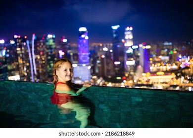 Children Swimming In Roof Top Outdoor Pool On Family Vacation In Singapore. City Skyline From Infinity Pool In Luxury Hotel. Kids Swim And Enjoy Skyscraper View In Asia. Travel With Young Child.