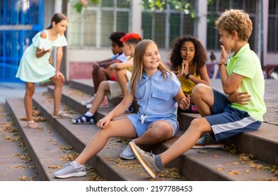 Children talking together while sitting on stairs outdoors. Youngsters chatting during summer day. - Shutterstock ID 2197788453