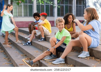 Children talking together while sitting on stairs outdoors. Youngsters chatting during summer day.