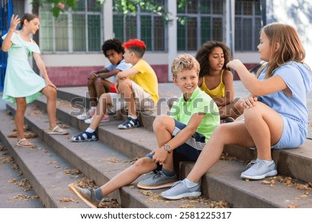 Children talking together while sitting on stairs outdoors. Youngsters chatting during summer day.