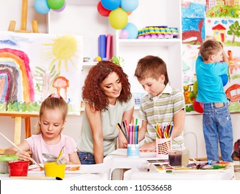 Children With Teacher Painting At Easel In School.