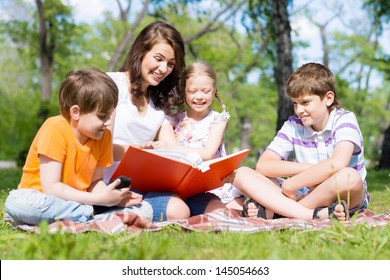 children and teacher reading book together in the summer park - Shutterstock ID 145054663
