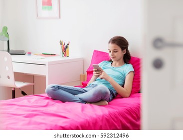children, technology and communication concept - smiling girl texting on smartphone and lying in bed at home