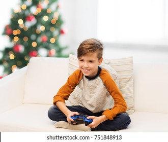 Children, Technology And People Concept - Smiling Boy With Gamepad Playing Video Game At Home Over Christmas Tree Background